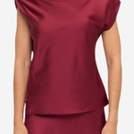 A woman wearing a draped off-the-shoulder satin top and matching skirt in a deep burgundy red, shown against a plain light gray studio background.