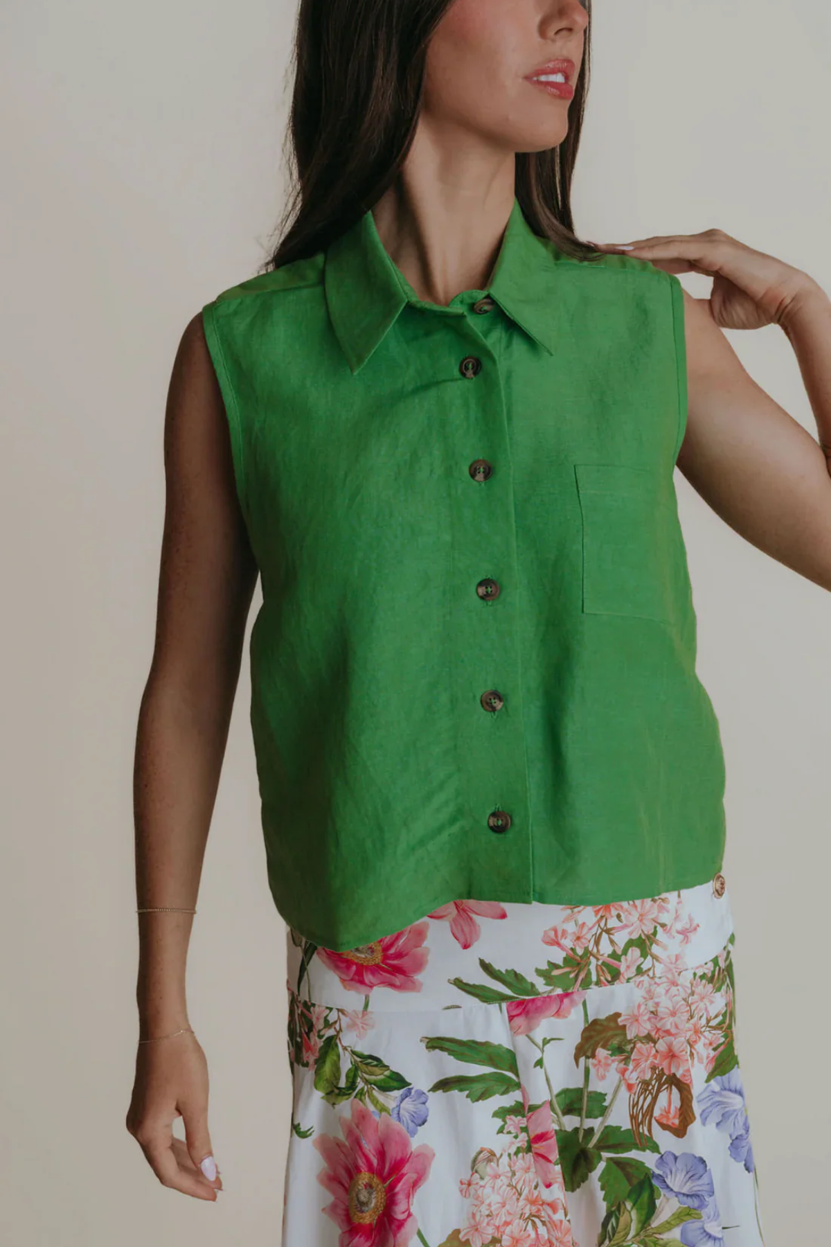 Woman wearing a green sleeveless shirt with a floral skirt against a neutral background