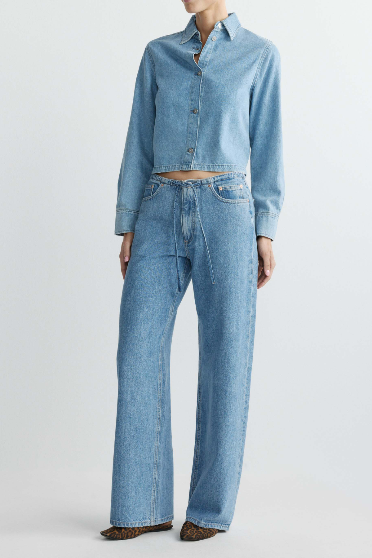 Person wearing a light blue denim shirt and jeans on a plain background