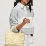 Woman holding a woven beige bag against a plain background