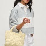 Woman holding a woven beige bag against a plain background