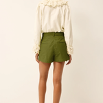 Woman wearing a white blouse with lace details and green shorts on a white background