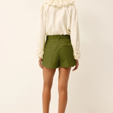 Woman wearing a white blouse with lace details and green shorts on a white background