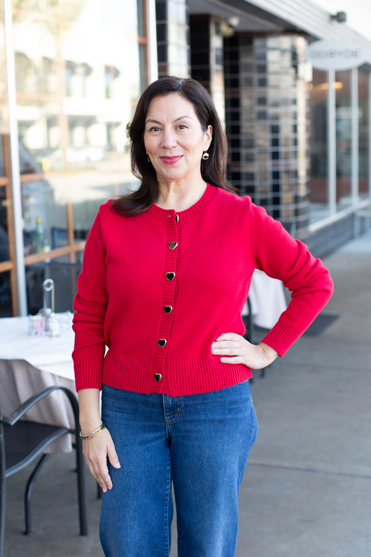 Woman wearing a red cardigan and blue jeans standing outdoors.