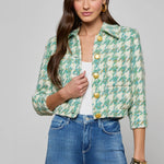Woman wearing a green floral jacket with yellow buttons and blue jeans on a gray background