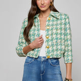 Woman wearing a green floral jacket with yellow buttons and blue jeans on a gray background