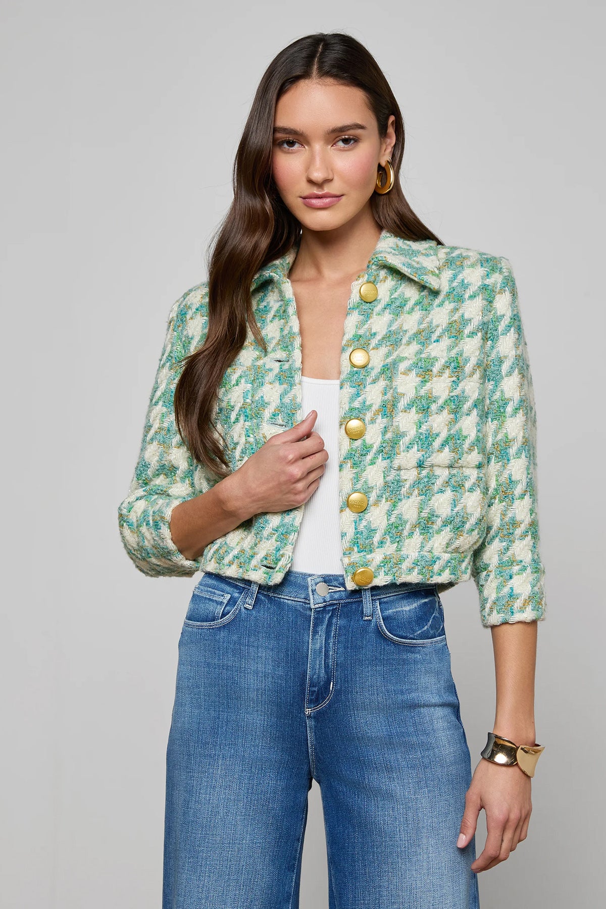 Woman wearing a green floral jacket with yellow buttons and blue jeans on a gray background