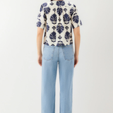 Person wearing a patterned shirt and light blue jeans on a white background