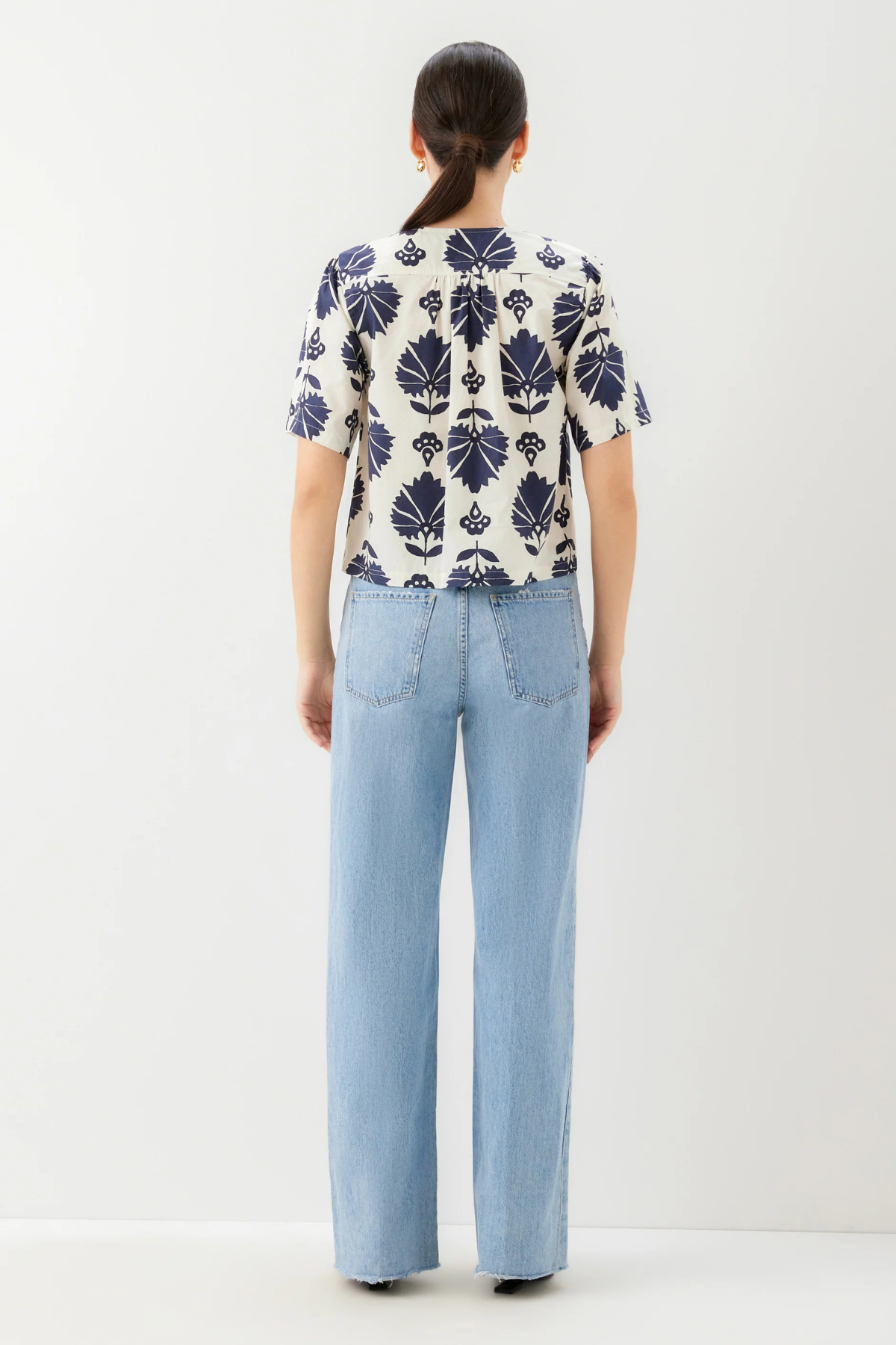 Person wearing a patterned shirt and light blue jeans on a white background