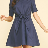 Woman wearing a navy blue dress with a tie waist on a beige background