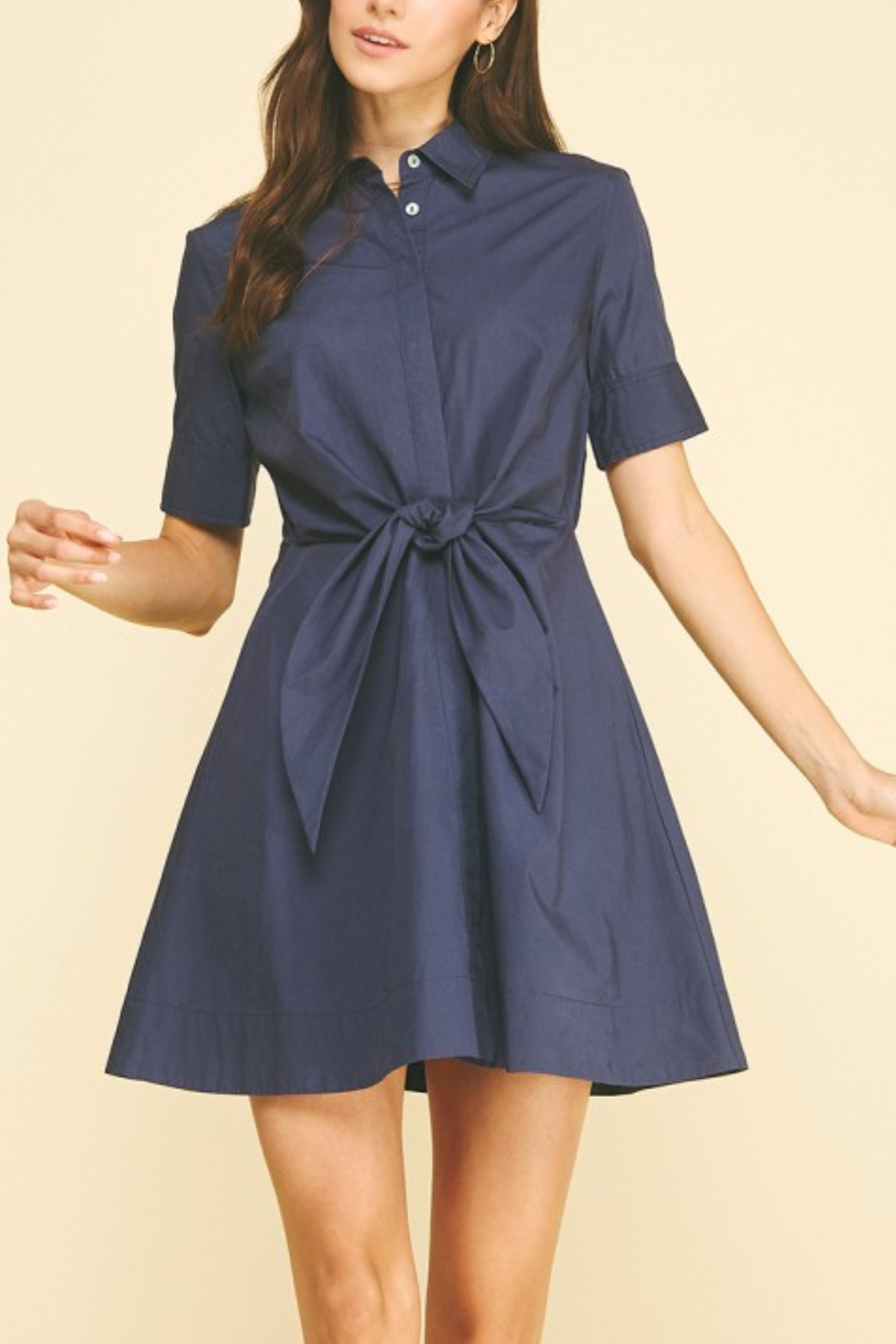 Woman wearing a navy blue dress with a tie waist on a beige background