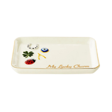 An off-white ceramic lucky tray with a gold rim, featuring small decorative charms including a green four-leaf clover, a blue and white evil eye, a red ladybug, and a white cat. The bottom right corner is inscribed with 'My Lucky Charm' in gold script.