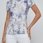 Woman wearing a floral patterned shirt and white pants on a plain background