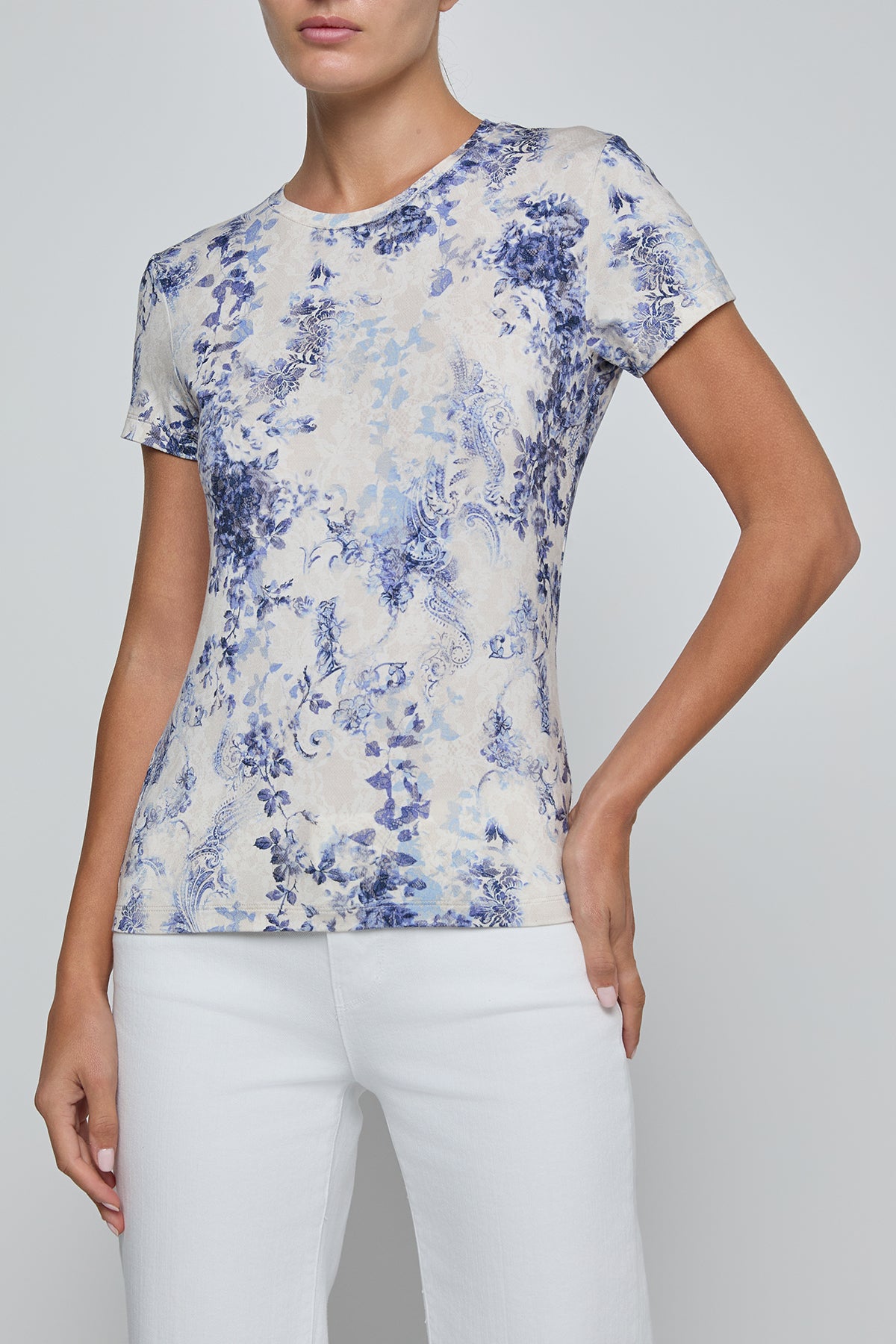 Woman wearing a floral patterned shirt and white pants on a plain background