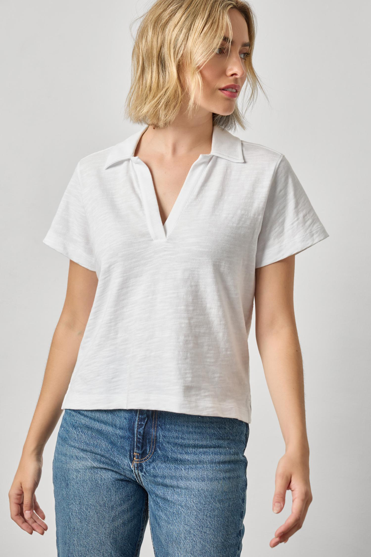 Woman wearing a white polo shirt and blue jeans on a plain background