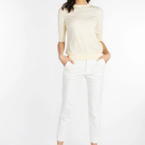 A woman modeling a cream-colored short-sleeve knit top and white cropped trousers with beige strappy heels, standing against a plain white studio background.