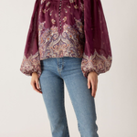 Person wearing a patterned blouse and jeans on a plain background