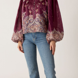 Person wearing a patterned blouse and jeans on a plain background