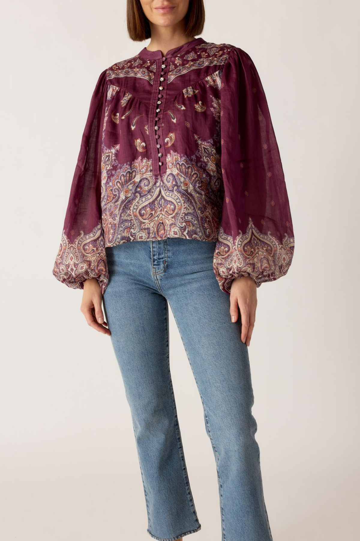 Person wearing a patterned blouse and jeans on a plain background