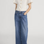 Person wearing a white blouse and blue jeans on a plain background