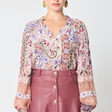 a model wearing a paisley printed long sleeve blouse with a burgundy skirt with buttons against a white background