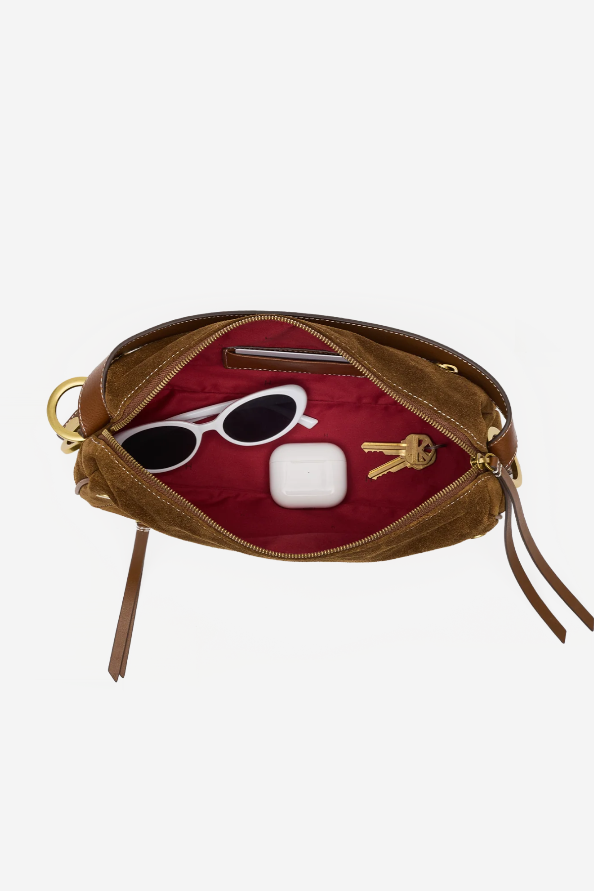 An open brown leather pouch or clutch with a deep red interior, shown on a light gray background. Inside, white sunglasses, a white earbud case, and two keys are arranged as props.