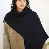 A woman wearing a large black shawl draped over her shoulders, layered over a beige suede jacket, against a clean white background.