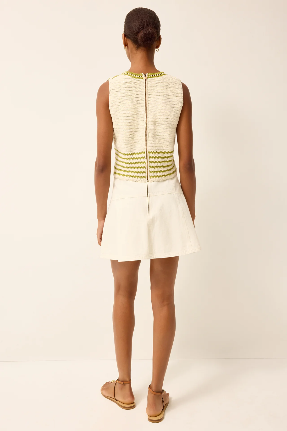 Woman wearing a white dress with green accents on a plain background