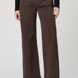 A model wearing a pair of dark brown wide-leg corduroy pants, styled with a black long-sleeve top and black leather clogs, against a light gray studio background.