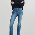 A model wearing a navy blue v-neck sweater, a white undershirt, blue cropped jeans, and black flats, standing with arms crossed against a light gray studio background.