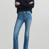 A model wearing a navy blue v-neck sweater, a white undershirt, blue cropped jeans, and black flats, standing with arms crossed against a light gray studio background.