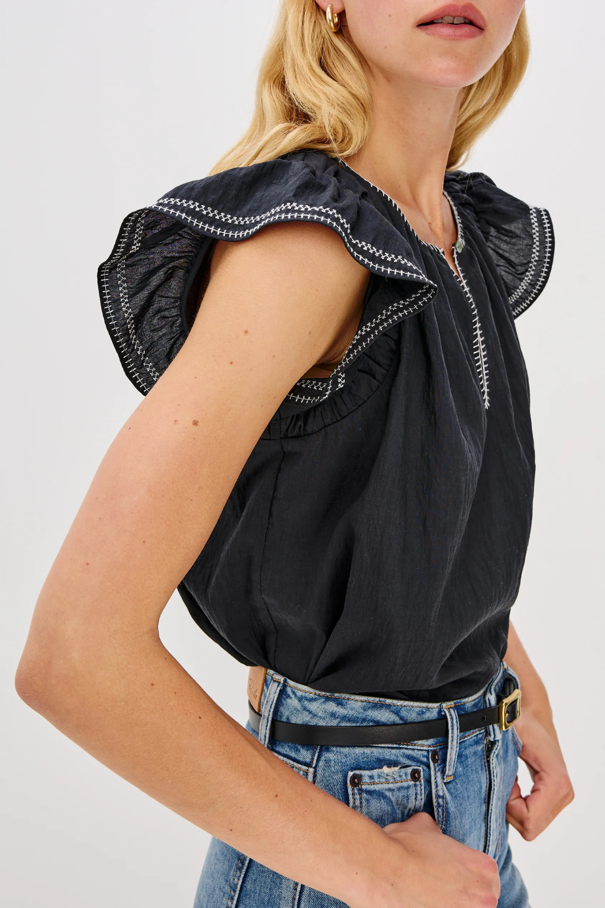 Black top with ruffled shoulders worn by a person on a white background