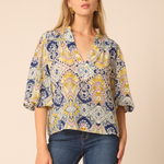 Woman wearing a patterned blouse and jeans on a beige background