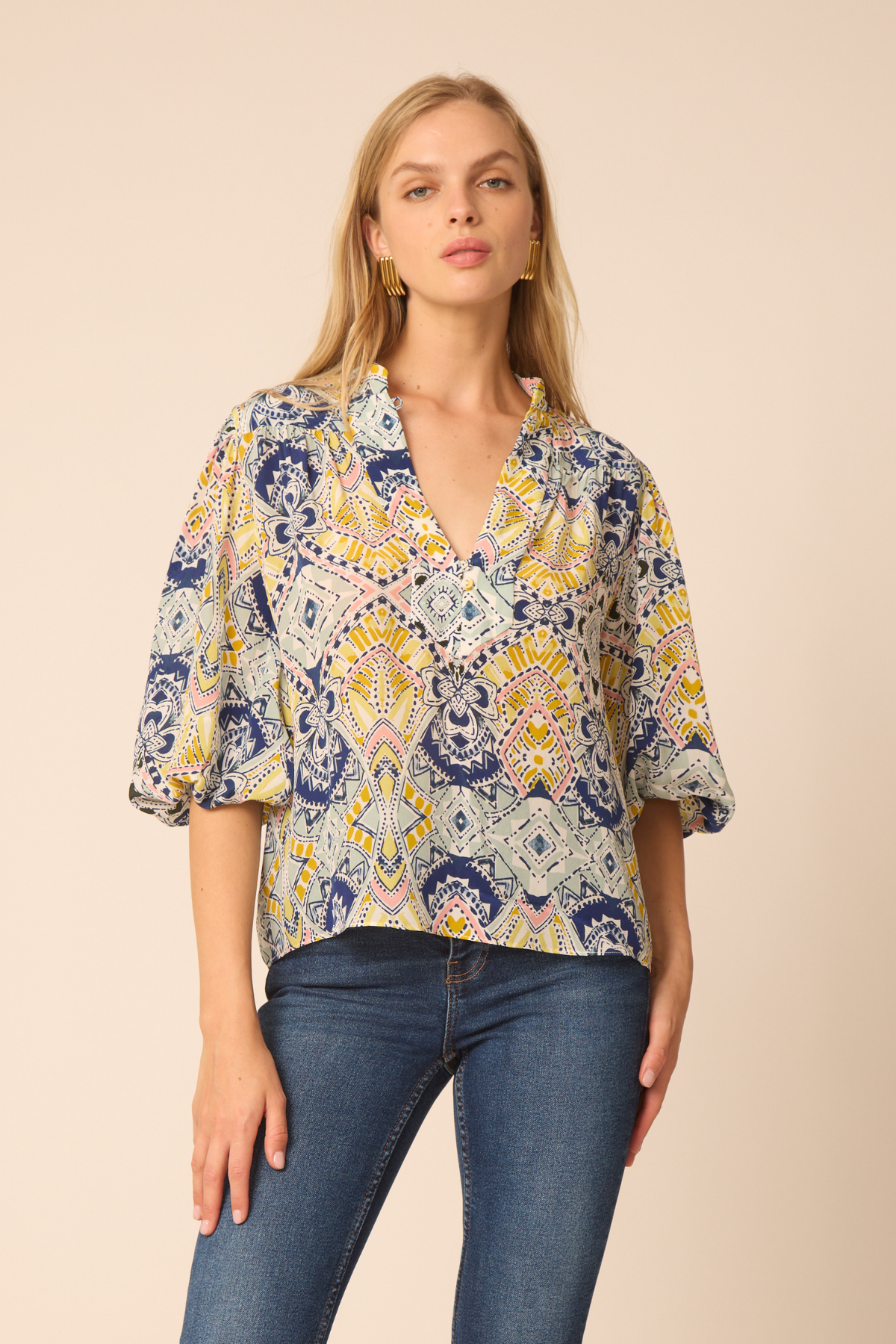 Woman wearing a patterned blouse and jeans on a beige background