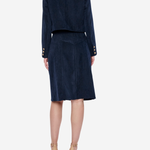A model shown from the back wearing a navy blue velvet two-piece set consisting of a cropped jacket with gold button details on the sleeves and a matching knee-length skirt, paired with beige high-heeled sandals against a light gray background.