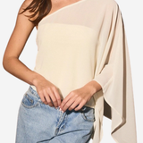 A woman wearing a light beige one-shoulder draped top and light blue jeans, shown from the neck down against a plain white background.
