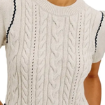 Close-up of a cream cable-knit short-sleeve top or dress with dark navy wavy trim along the shoulders and waist, worn by a model.