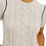 Close-up of a cream cable-knit short-sleeve top or dress with dark navy wavy trim along the shoulders and waist, worn by a model.