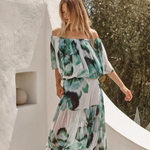 Woman wearing a floral dress standing against a white wall with greenery in the background