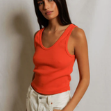 Woman wearing an orange tank top and white pants against a plain background