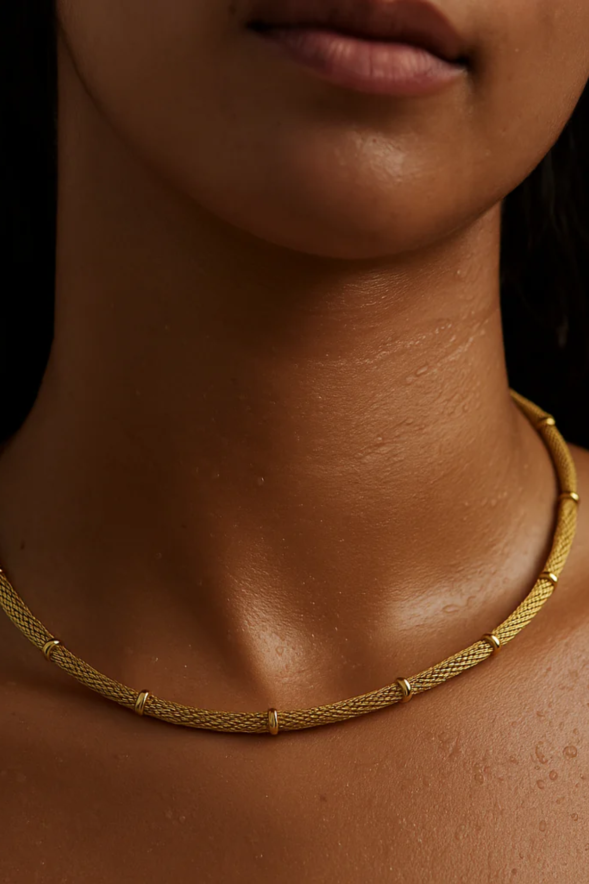 Close-up of a person wearing a gold necklace against a dark background