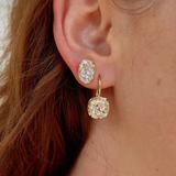 Close-up of a person's ear wearing a pair of gold hoop earrings with cushion-cut clear gemstones.