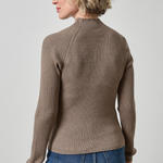 Woman wearing a brown ribbed sweater and blue jeans on a plain background