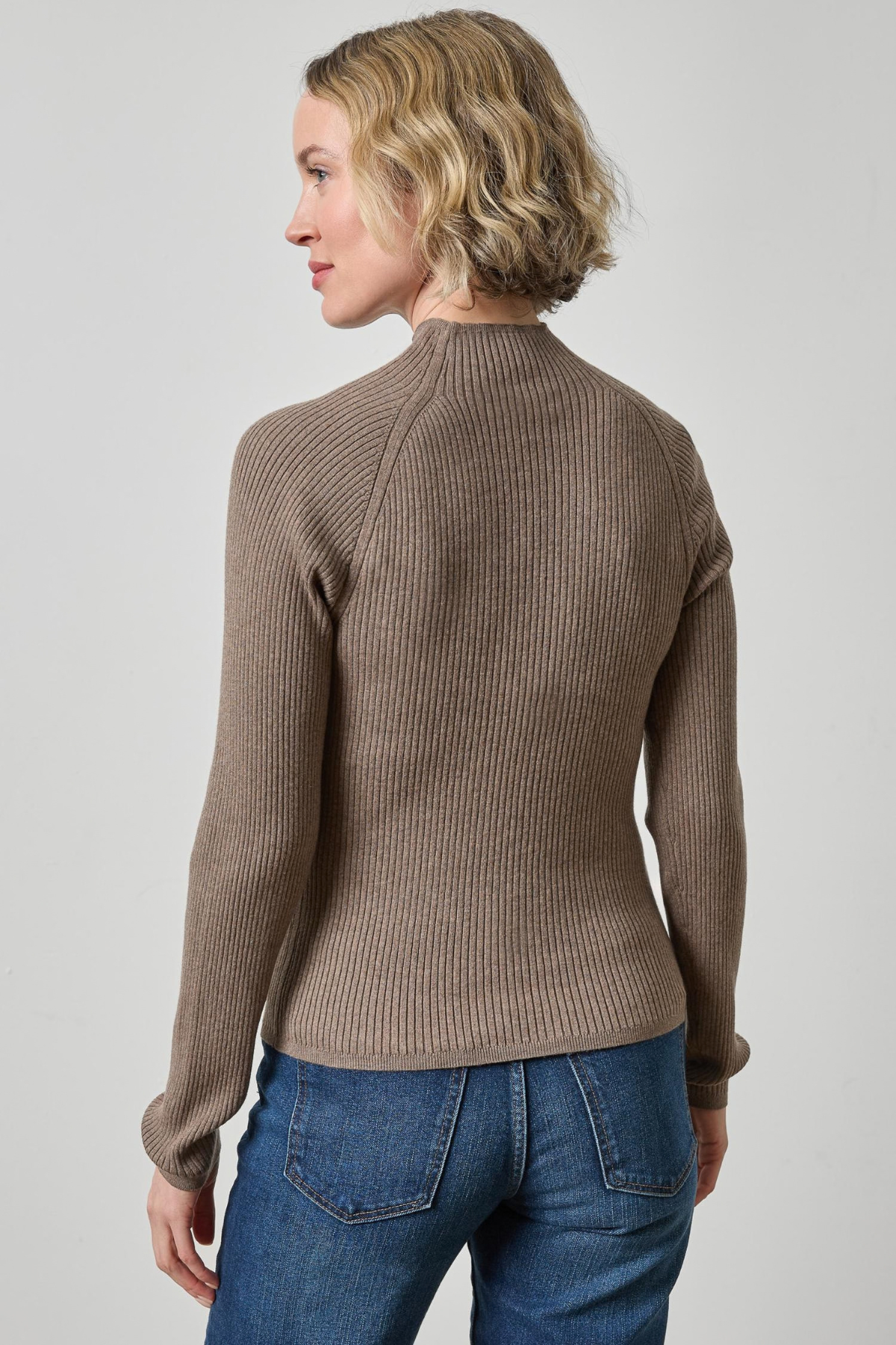 Woman wearing a brown ribbed sweater and blue jeans on a plain background