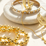 Gold jewelry including bracelets and a necklace on a white dish.