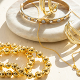 Gold jewelry including bracelets and a necklace on a white dish.