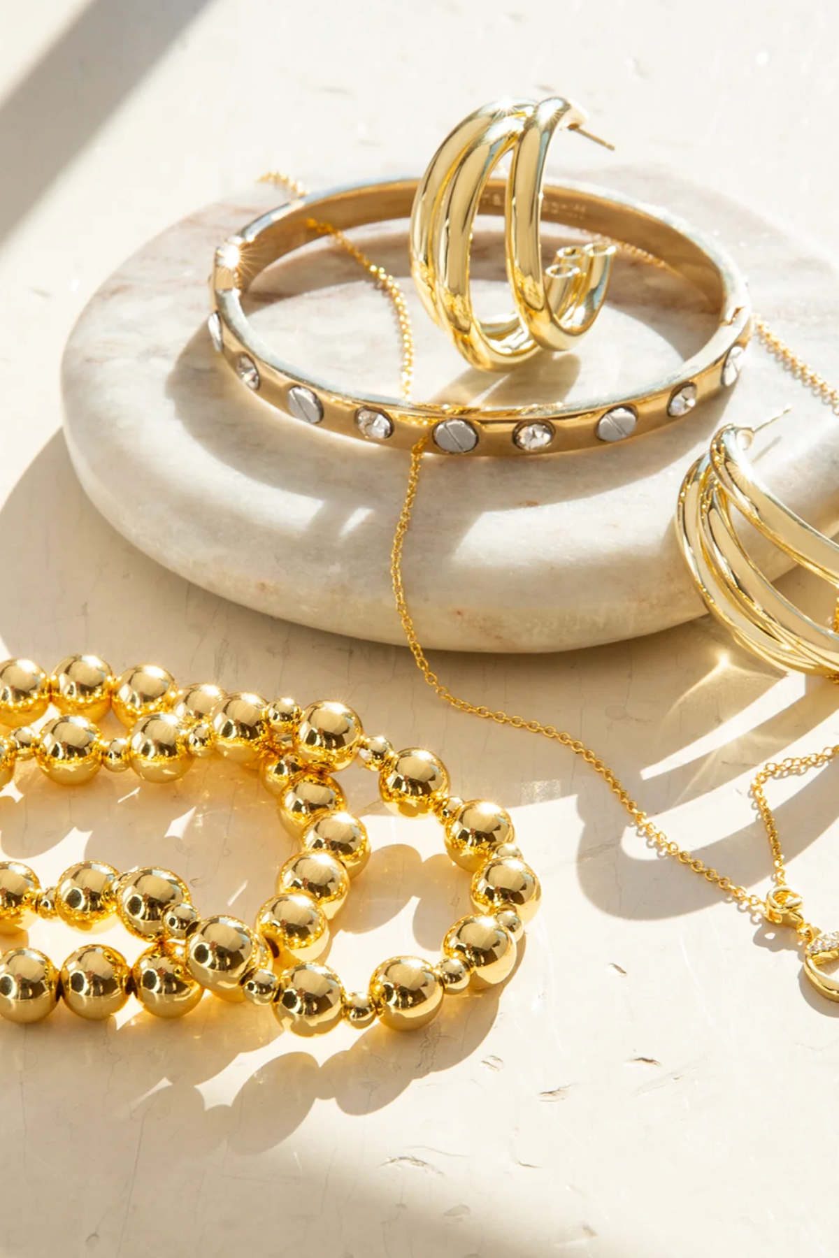 Gold jewelry including bracelets and a necklace on a white dish.