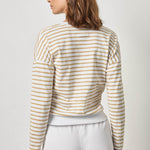 Woman wearing a striped long-sleeve top and white pants on a plain background