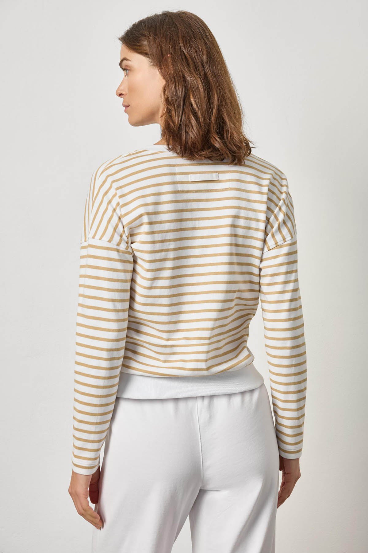 Woman wearing a striped long-sleeve top and white pants on a plain background