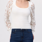 Woman wearing a white lace cardigan over a white top and blue jeans on a white background